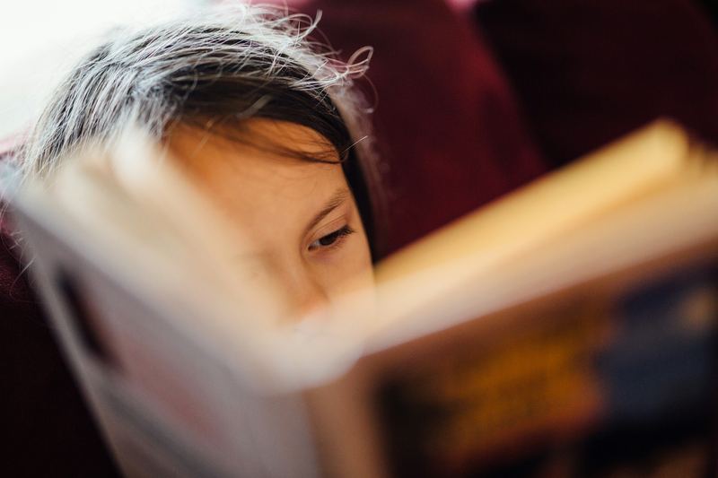 Menina lendo com o livro bem perto do rosto